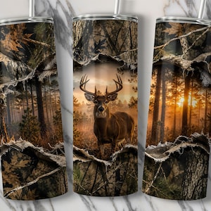 May include: A cylindrical tumbler featuring a wrap-around design of a buck with large antlers standing in a forest at sunset. The graphic includes a camouflage pattern with a torn-paper effect revealing the deer and pine trees in warm light.