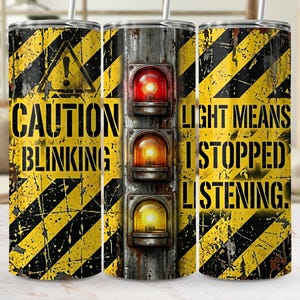 May include: A cylindrical tumbler featuring a yellow and black diagonal hazard stripe pattern with a distressed, weathered texture. The design includes a vertical traffic light graphic and the text CAUTION BLINKING LIGHT MEANS I STOPPED LISTENING.