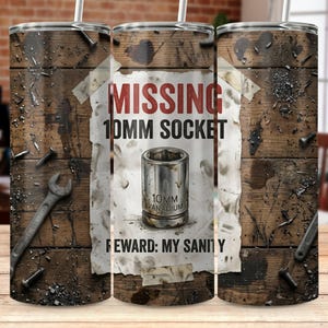 Può includere: Un bicchiere in acciaio inossidabile con un design a venature di legno invecchiato. Il bicchiere presenta un foglio con le parole "MISSING 10MM SOCKET" e l'immagine di una presa. È visibile anche il testo "REWARD: MY SANITY".
