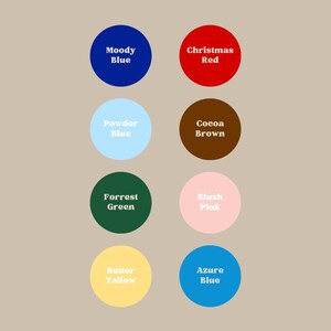 Op de afbeelding: Een kleurenpalet met acht cirkelvormige kleurstalen op een neutrale achtergrond. De kleuren zijn Moody Blue, Christmas Red, Powder Blue, Cocoa Brown, Forrest Green, Blush Pink, Butter Yellow en Azure Blue, elk met hun naam.