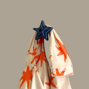 May include: A blue star-shaped decorative object holds a cream-coloured fabric with a repeating orange star pattern. The fabric appears to be part of a garment, possibly a jacket or a robe.