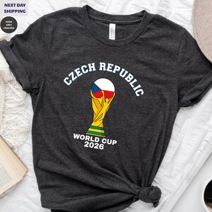 May include: A white ceramic mug with a black handle and the text "But First, Coffee" in a bold, black font. The mug is set against a blurred background, suggesting a cozy setting.