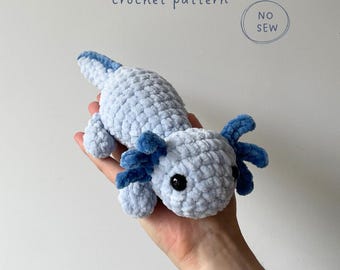 Op de afbeelding: Een lichtblauw en donkerblauw gehaakt axolotl knuffeltje met zwarte ogen. De tekst luidt Moochie the axolotl crochet pattern, NO SEW, en DESIGNED BY OCEAN FRIENDS CROCHET. De knuffel heeft een zachte, getextureerde garen afwerking en een lange staart.