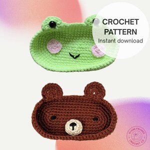 Puede incluir: Dos bandejas de ganchillo: una bandeja verde con forma de rana con detalles rosas y una bandeja marrón con forma de oso con nariz blanca. La imagen incluye el texto "CROCHET PATTERN Instant download" y el logo Ocean Friends Crochet Co.