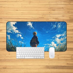 Puede incluir: Alfombrilla de escritorio rectangular con un personaje de anime en un campo bajo un cielo azul con nubes. Un teclado y un ratón blancos están en primer plano, sobre una superficie de madera.