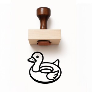 May include: A wooden rubber stamp with a dark brown handle and a light brown base. The stamp imprint is a black and white outline of a duck with a life preserver.