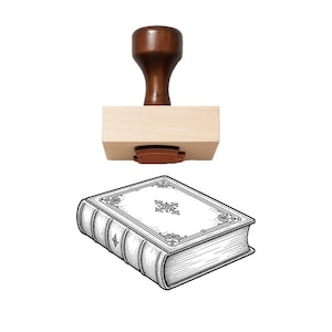 May include: A wooden rubber stamp featuring a dark brown handle and a light-colored rectangular base. Below the stamp is a black and white line art illustration of a closed, thick book with ornate decorative borders and a central floral motif.