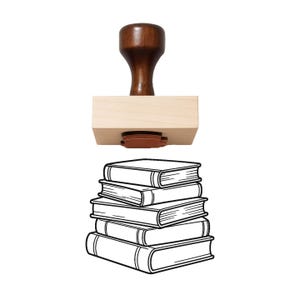 May include: A wooden rubber stamp featuring a dark brown handle and a light tan rectangular base. The stamp die displays a black line art illustration of a stack of five books, showing the spines and covers in a simple, clean graphic style.