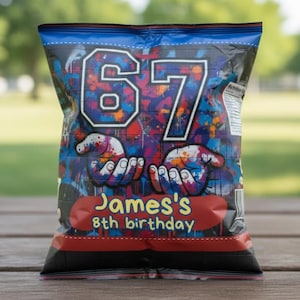 Op de afbeelding: Een kleurrijke chipszak met het witte nummer 67, omgeven door een graffiti-stijl ontwerp. De zak heeft de tekst "James's 8th birthday" op een rode banner. De zak staat op een houten tafel met een vage groene achtergrond.