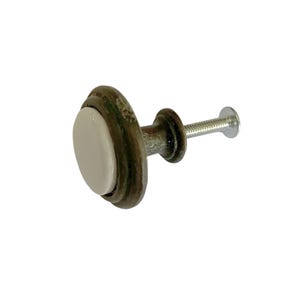 May include: A round cabinet knob featuring a smooth, white circular center inlay surrounded by a weathered, dark bronze-toned metal frame with a visible patina. The knob includes a threaded metal bolt extending from the back for installation.