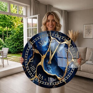 May include: A large circular wall clock featuring a deep blue and gold marbled pattern across the face. The clock has gold-colored hands and classic Roman numerals in gold, arranged around a detailed gold-lined border on a dark blue background.