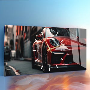 May include: A rectangular wall clock featuring a high-gloss print of a red sports car parked on a city street. The clock face is integrated into the image with white hour markers and thin gold-colored hands centered over the car's front hood.