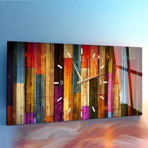 Peut inclure: Une horloge murale rectangulaire présentant un motif de planches de bois verticales multicolores aux tons rouge, bleu, jaune et violet. Le cadran comporte des marqueurs d'heures blancs, des aiguilles dorées et les chiffres 3, 6, 9 et 12.