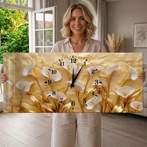 May include: A rectangular wall clock featuring a textured gold background with white calla lily flowers and gold stems. The clock face displays black Arabic numerals from 1 to 12 arranged in a circular pattern, with black hour and minute hands at the center.