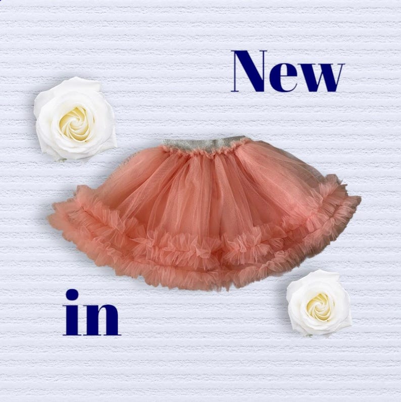Puede incluir: Falda de tul color coral con dobladillo con volantes, sobre un fondo blanco texturizado. Las palabras "New" e "in" se muestran encima y debajo de la falda. Dos rosas blancas se colocan a cada lado.