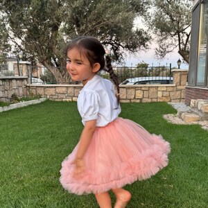 Puede incluir: Una ni&ntilde;a con una camiseta blanca de manga corta y una falda tut&uacute; rosa, girando en un c&eacute;sped verde. La falda es en capas y voluminosa. La ni&ntilde;a tiene el pelo oscuro y est&aacute; descalza.