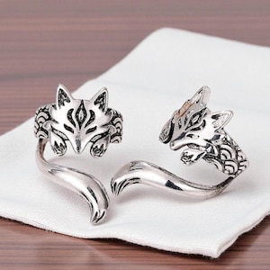 Peut inclure: Deux bagues argentées ornées de têtes de renard finement détaillées. Les bagues présentent un design de queue enroulée. Elles sont présentées sur un tissu blanc.
