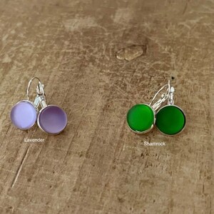 May include: Two pairs of earrings with silver hooks and round glass stones. One pair has lavender stones and the other pair has shamrock green stones.