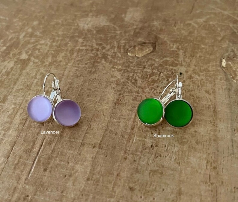 May include: Two pairs of earrings with silver hooks and round glass stones. One pair has lavender stones and the other pair has shamrock green stones.
