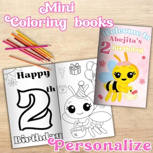 Op de afbeelding: Mini kleurboeken met de tekst "Happy 2nd Birthday" en "Welcome to Abejita's Birthday". De boeken bevatten illustraties van een bij en feestthema-afbeeldingen. Kleurpotloden liggen in de buurt van de boeken.