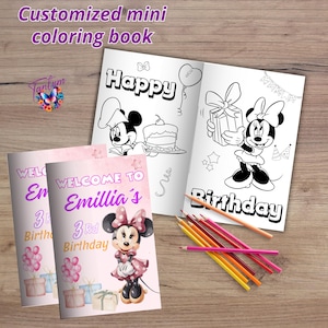 Op de afbeelding: Een aangepast mini kleurboek met de tekst "Customized mini coloring book" bovenaan. Het open boek bevat een Minnie Mouse-illustratie met de woorden "Happy" en "Birthday". Twee roze boekjes zeggen "Welcome to Emillia's 3rd Birthday". Kleurpotloden liggen verspreid op een houten oppervlak.