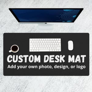 Puede incluir: Alfombrilla de escritorio negra personalizada con teclado, ratón y taza de café blancos. La alfombrilla tiene el texto "CUSTOM DESK MAT" y "Add your own photo, design, or logo" en blanco.