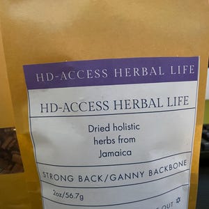 May include: A tan paper bag with a white label featuring the text "HD-ACCESS HERBAL LIFE." The label also states "Dried holistic herbs from Jamaica" and "STRONG BACK/GANNY BACKBONE." The bag contains 2oz/56.7g of herbs.