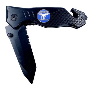May include: Black folding knife with a partially serrated blade. The handle is black with a textured grip and a blue and white circular emblem that reads "CERTIFIED DRONE PILOT". The knife also features a seat belt cutter and a glass breaker.