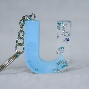 May include: A light blue resin letter "U" keychain with silver flakes and a silver chain. The letter is partially translucent, with a solid blue base and clear top. The keychain is a decorative accessory.