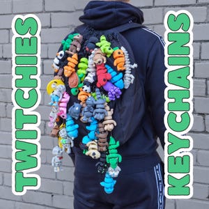 May include: A black backpack adorned with numerous small, brightly coloured keychains. The keychains depict diverse shapes and characters. The words "TWITCHIES" and "KEYCHAINS" are displayed vertically on either side of the image in green text.