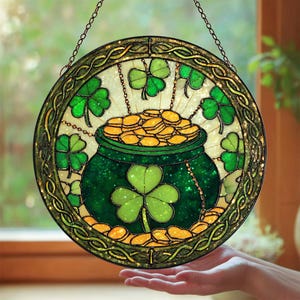May include: Round stained glass decoration featuring a green pot filled with gold coins, surrounded by green shamrocks. The pot is centered, with shamrocks around the edge. The border is a decorative gold color, and the piece hangs from a chain.