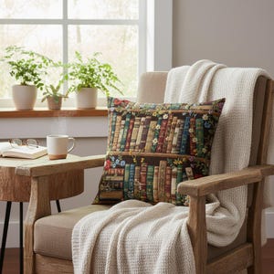 Peut inclure: Un coussin décoratif avec une impression détaillée d'une bibliothèque remplie de livres colorés. Le coussin est placé sur un fauteuil en bois avec une couverture crème. Une tasse de café est posée sur une table d'appoint à côté d'un livre ouvert et de lunettes.