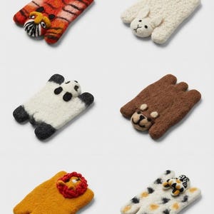 May include: A selection of felt animal-shaped coasters. The coasters depict a tiger, rabbit, panda, bear, lion, and a cat. Each coaster has a unique colour scheme and animal face detail.