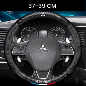 Op de afbeelding: Zwarte stuurwielhoes met koolstofvezeltextuur, ontworpen voor een perfecte pasvorm. De hoes is voorzien van het opschrift "MITSUBISHI" en past op stuurwielen van 37-39 cm. De afbeelding toont de hoes op een autostuur.