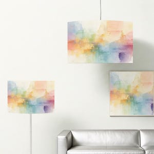 Può includere: Tre paralumi e una stampa incorniciata con un design ad acquerello. I paralumi sono rettangolari e cilindrici, e la stampa è quadrata. L'opera presenta sfumature miste di arancione, giallo, blu e viola.