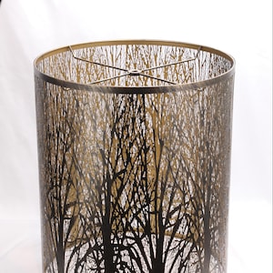 Puede incluir: Pantalla de lámpara cilíndrica con diseño de ramas de árbol. La pantalla de metal tiene un acabado bronce, con ramas de árbol negras sobre un fondo dorado. Tiene un marco de metal en la parte superior e inferior. Diámetro aproximado de 30 cm.