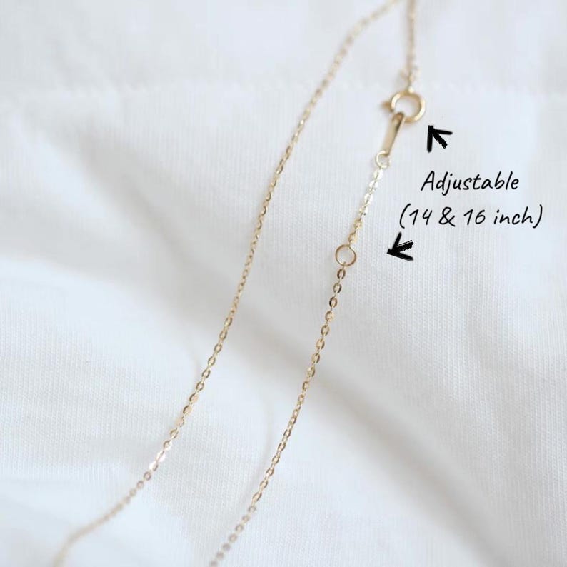 Peut inclure: Un collier en or d&eacute;licat avec une longueur r&eacute;glable, pr&eacute;sent&eacute; sur un fond blanc. Le texte indique que le collier peut &ecirc;tre ajust&eacute; &agrave; 35,5 ou 40,6 cm. La cha&icirc;ne est fine et le fermoir est visible.