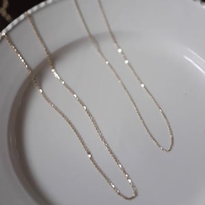 Peut inclure: Deux colliers en or d&eacute;licats avec de fines cha&icirc;nes sont pr&eacute;sent&eacute;s sur une assiette blanche. Les colliers ont un &eacute;clat subtil, captant la lumi&egrave;re. Les cha&icirc;nes sont fines et &eacute;l&eacute;gantes, sugg&eacute;rant un style de bijoux minimaliste.