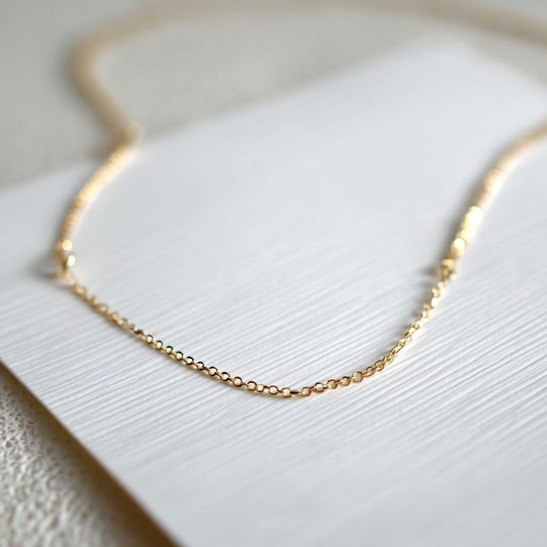 Peut inclure: Un collier d&eacute;licat de couleur or avec une fine cha&icirc;ne. Le collier est pr&eacute;sent&eacute; sur une surface blanche textur&eacute;e. La cha&icirc;ne est compos&eacute;e de petits maillons reli&eacute;s, cr&eacute;ant un design simple et &eacute;l&eacute;gant. Le collier est un bijou.
