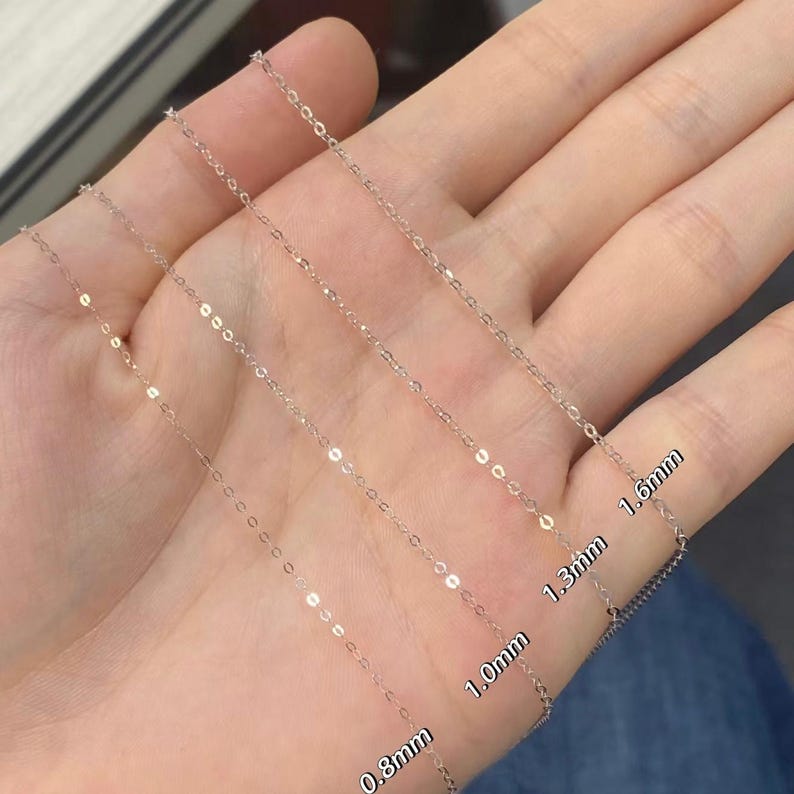 Peut inclure: Gros plan sur quatre colliers en cha&icirc;ne argent&eacute;s de diff&eacute;rentes &eacute;paisseurs : 0,8 mm, 1,0 mm, 1,3 mm et 1,6 mm. Les cha&icirc;nes sont pr&eacute;sent&eacute;es sur un fond clair, mettant en valeur leurs d&eacute;tails fins et leurs surfaces r&eacute;fl&eacute;chissantes. L'image met en &eacute;vidence les diff&eacute;rents styles de cha&icirc;nes.