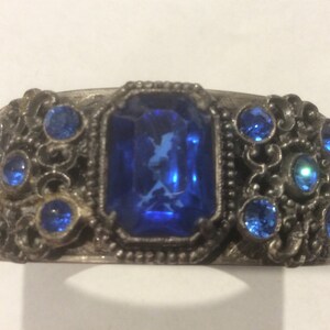May include: A silver bracelet with a large blue gemstone surrounded by smaller blue gemstones.