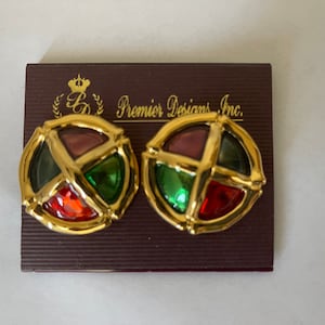 May include: A pair of gold tone earrings with a round, multi-colored glass design. The earrings are on a brown card with the text "Premier Designs Inc."