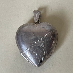 Peut inclure: Un médaillon en argent en forme de cœur avec un motif floral gravé. Le médaillon a une ouverture à charnière et une boucle pour attacher une chaîne.