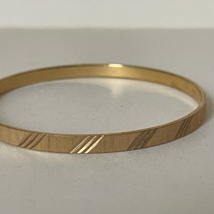 May include: A gold bangle bracelet with a simple, textured design.