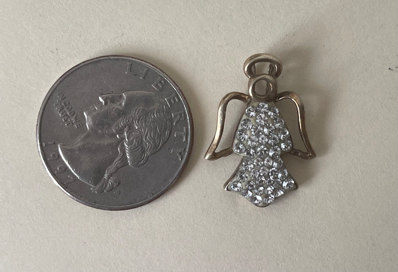 May include: A silver angel charm with clear rhinestones. The charm is about the size of a 20 pence coin.