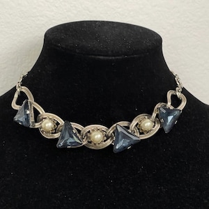 May include: A silver chain necklace with dark blue triangular-shaped stones and white pearl accents.