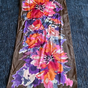 May include: A brown silk scarf with a floral print in shades of pink, orange, purple, and white. The scarf has the text "Cynthia Rowley" printed in white on the bottom right corner.