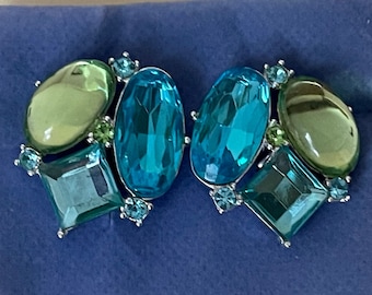 May include: A pair of silver tone earrings with a cluster of blue and green gemstones. The earrings feature a large oval shaped blue gemstone, a smaller square shaped green gemstone, and a round green gemstone.