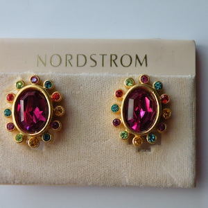 May include: A pair of gold earrings with a pink oval-shaped stone surrounded by a circle of colorful stones. The earrings are on a white card with the word "Nordstrom" printed on it.