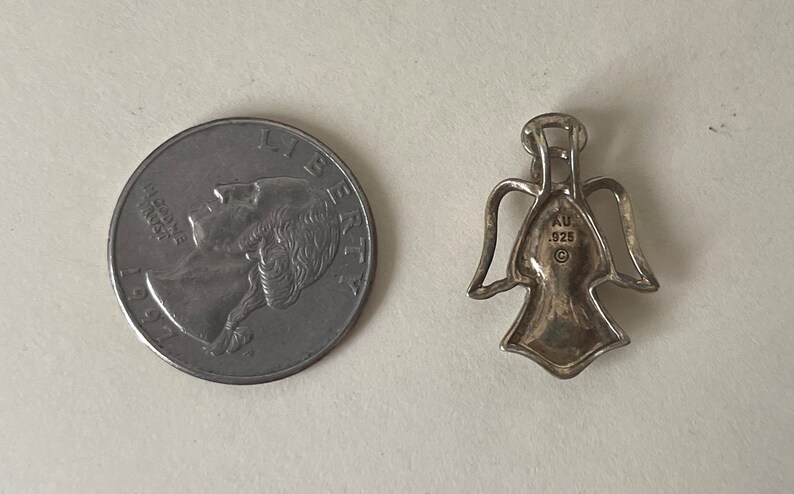 May include: Silver angel pendant charm with a hallmark that reads "AU .925" on the back.